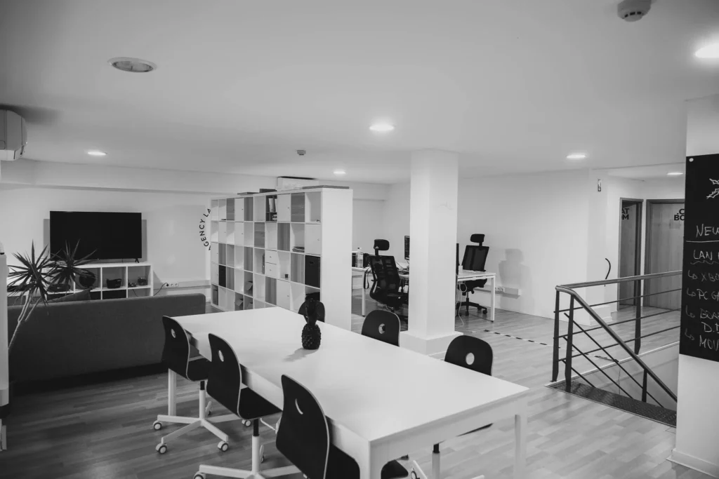 Interior de escritório espaçoso e elegante em monocromático na Lava, com uma grande mesa de trabalho comunitária com cadeiras modernas e um quadro-negro, indicativo de um ambiente colaborativo de web e branding.